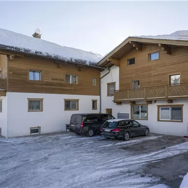 A building in the snow with two houses on top of it. In front of the houses, several cars are parked on a frozen surface.