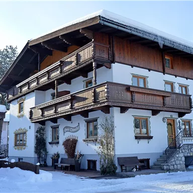 Ein charmantes Gebäude im alpinen Stil, umgeben von Schnee. Die Fassade zeigt Holzbalkone und rustikale Details.