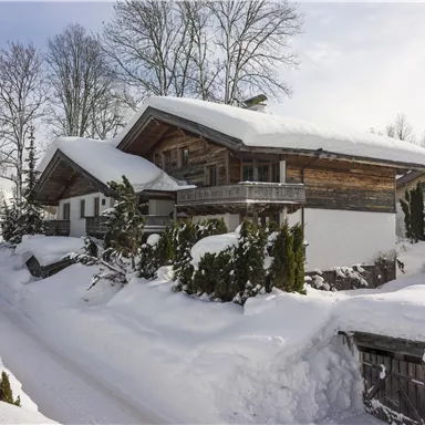 Ein gemütliches Holzhaus im Schnee, umgeben von Bäumen. Die Landschaft ist winterlich und friedlich.