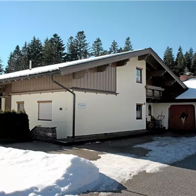 A modern house in a snow-covered landscape. In the background, high trees and blue sky can be seen.