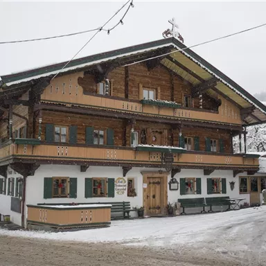 Ein traditionelles Holzhaus in einem verschneiten Dorf. Die gesamte Umgebung ist mit Schnee bedeckt, und die Architektur ist typisch für alpine Regionen.