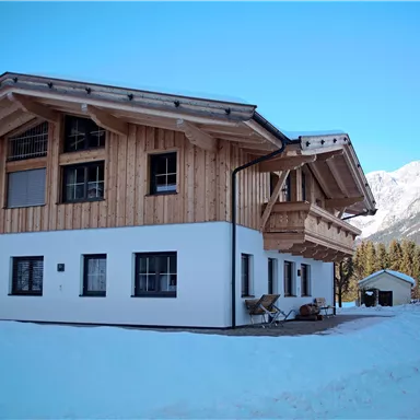 A modern wooden house with a white base in a snowy landscape. Snow-covered mountains can be seen in the background.