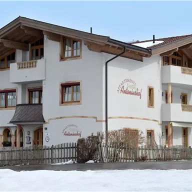 Ein hübsches Gebäude im alpinen Stil, umgeben von Schnee. Die Fassade ist hell mit Holzverzierungen und klassischen Fenstern.