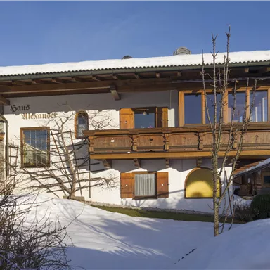 A charming house in alpine style, surrounded by snow. The sky is clear and blue, creating a serene winter atmosphere.