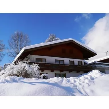 A cozy house in the snow with a clear blue sky. The surroundings are wintry with a lot of fresh snow.