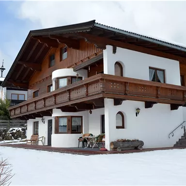 Ein wunderschönes Haus im alpinen Stil, umgeben von Schnee. Der Balkon aus Holz und die Fenster verleihen dem Gebäude einen charmanten Charakter.