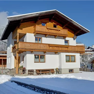 Ein gemütliches Haus im Bergstil, umgeben von Schnee. Der Himmel ist klar und blau, was die winterliche Atmosphäre verstärkt.