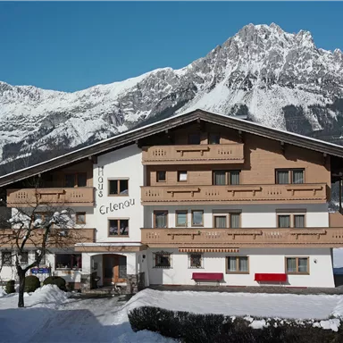 A charming multi-storey alpine house in winter. In the background, majestic mountains rise up, while the ground is covered with snow.