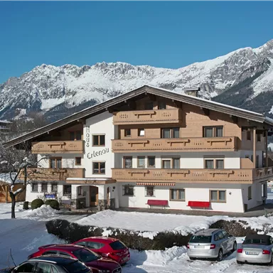 A charming hotel in a snow-covered landscape. In the background, majestic mountains and a clear blue sky can be seen.