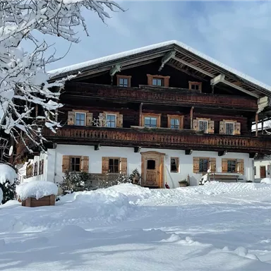 A traditional wooden house in the snow, surrounded by a wintry landscape. The sky is partially cloudy and the surroundings are quiet and peaceful.