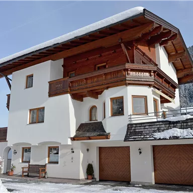 Ein modernes Haus im Alpinstil, umgeben von Schnee. Der Balkon und die Holzverkleidung verleihen ihm einen charmanten Charakter.