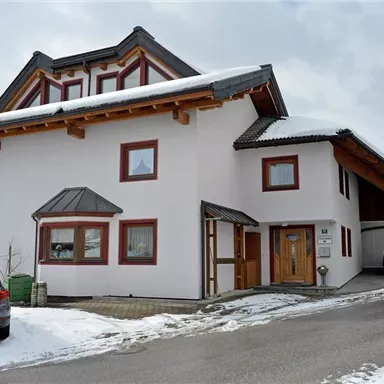 Ein modernes Haus in den Bergen, umgeben von Schnee. Die Fassade ist weiß mit Holzdetails und großen Fenstern.