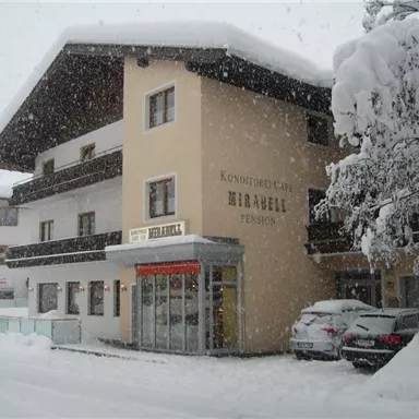 Ein gemütliches Pension-Haus im Schnee mit einem großen, schneebedeckten Dach. Die Umgebung ist winterlich und malerisch.