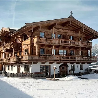 A beautiful alpine wooden house, surrounded by snow and mountains. The architecture is traditional with balconies and wooden decorations.