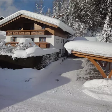 Ein gemütliches Haus im Schnee, umgeben von einer winterlichen Landschaft. Die schneebedeckten Dächer und Bäume schaffen eine ruhige Atmosphäre.