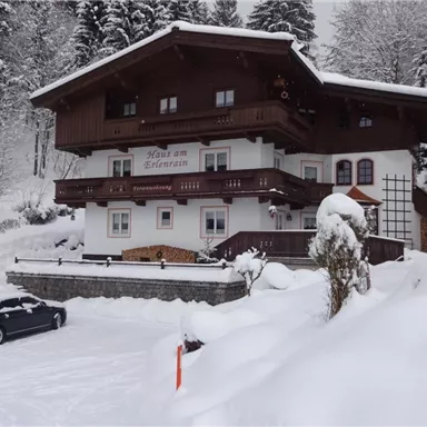 A cozy house in the snow with a balcony and wooden cladding. Surrounded by snow-covered trees and a tranquil winter landscape.