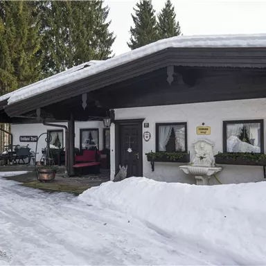 A cozy house in the snow with a snow-covered front yard. Surrounded by tall trees, it radiates a calm winter atmosphere.