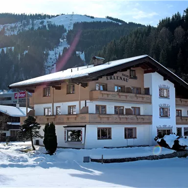 A cozy hotel in the winter snow with snow-covered mountains in the background. The facade is bright and inviting, surrounded by snow-covered trees.