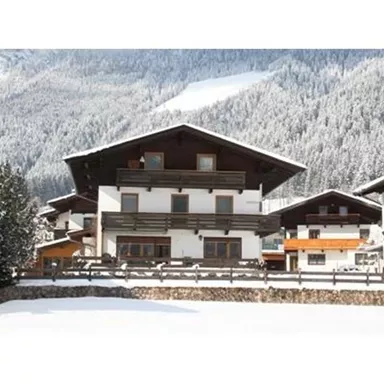 Ein gemütliches Ferienhaus im Schnee, umgeben von verschneiten Bergen. Die Architektur ist traditionell mit einem Holzgeländer und großen Fenstern.
