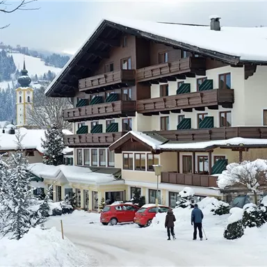A picturesque hotel in the snow with snow-covered trees. In the background, mountains and a church can be seen.