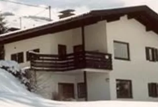 A modern house in a snowy landscape. Surrounded by trees and mountains, the scenery creates a calm, wintry atmosphere.