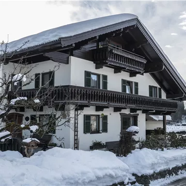 A traditional house in Bavarian style, surrounded by snow. The sky is cloudy and the surroundings appear calm and picturesque.