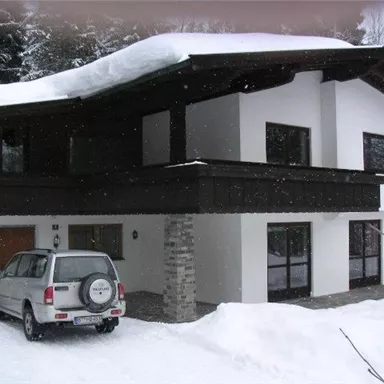 A modern house in the snow with a green roof. A car is parked in the driveway in front of the building.