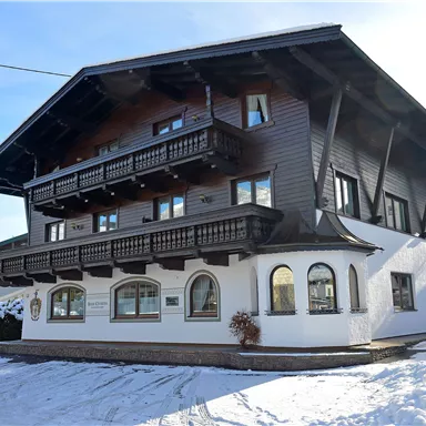 A charming building in alpine style with several balconies. It stands in a snow-covered landscape under a clear sky.