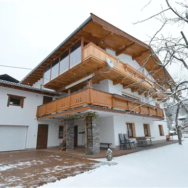 Ein modernes Haus im Schnee mit einem großen Balkon aus Holz. Die Umgebung ist ruhig und malerisch, ideal für einen Winteraufenthalt.