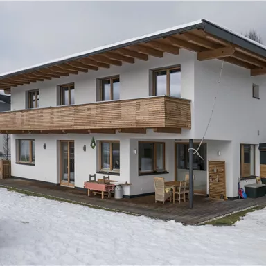 A modern house with wood siding and a spacious balcony. It is located in a winter landscape with snow.