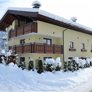 Ein gemütliches Haus im Winter, umgeben von Schnee. Die Balkone und die Landschaft schaffen eine einladende Atmosphäre.