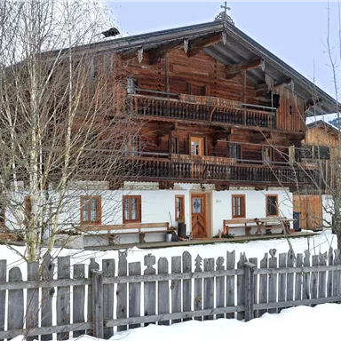 Ein traditionelles Chalet aus Holz, umgeben von Schnee. Das Gebäude hat mehrere Balkone und eine schöne Holzumzäunung.