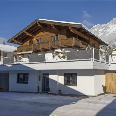 A modern chalet in the mountains, surrounded by snow. The clear skies and the mountain landscape create a peaceful atmosphere.
