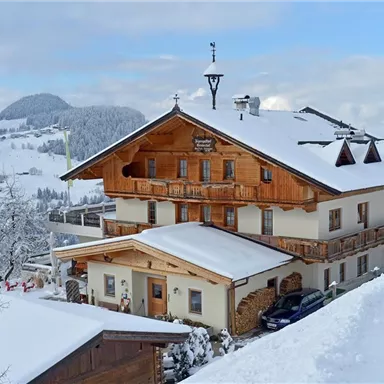 Ein charmantes, traditionelles Haus im Winter mit einer schneebedeckten Landschaft. Die Umgebung zeigt sanfte Hügel und einen klaren Himmel.
