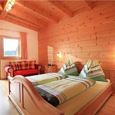 Ein helles Schlafzimmer mit Holzverkleidung und großzügigem Fenster. Das Zimmer ist gemütlich eingerichtet mit einem Doppelbett und einer Sitzecke.