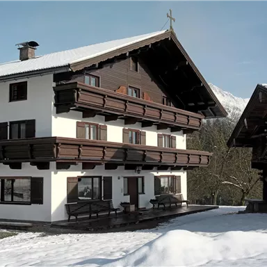 Ein traditionelles Alpenhaus mit schneebedecktem Dach. Die Umgebung ist winterlich und friedlich.