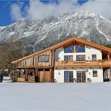 A beautiful chalet amidst a snowy landscape. In the background, impressive mountains rise under a clear sky.