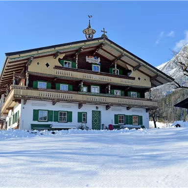 A traditional chalet surrounded by snow and mountains. The facade is designed in light colors with green shutters.