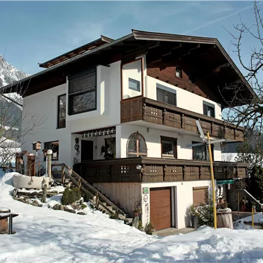 A charming house in alpine style, surrounded by snow. The architecture features traditional balconies and an inviting atmosphere.