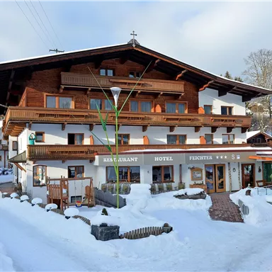 Ein charmantes Hotel im Alpenstil, umgeben von schneebedeckten Landschaften. Die Fassade ist aus Holz und verleiht dem Gebäude eine gemütliche Atmosphäre.