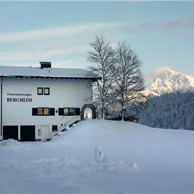 A picturesque holiday home in the snow named "Bergheim". In the background, snow-covered mountains and a clear sky can be seen.