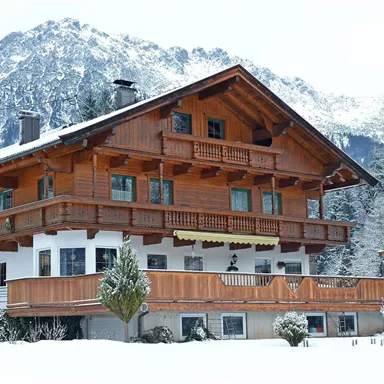 Ein charmantes Holzhaus im Schnee, umgeben von Bergen. Der Balkon ist mit Holzverzierungen und Pflanzen geschmückt.