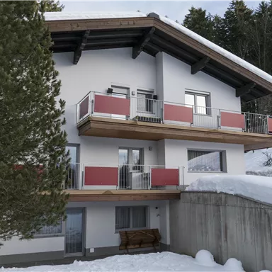 Ein modernes Gebäude im Schnee mit Balkonen. Umgeben von Bäumen und einer ruhigen Winterlandschaft.