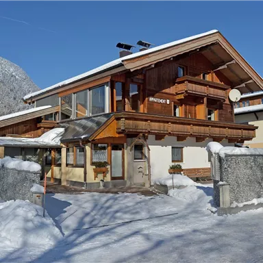 Ein schönes Holzhaus im Winter mit schneeüberdecktem Gelände. Der Himmel ist klar und blau.
