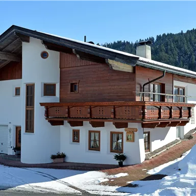 A beautiful chalet in the snow with a wooden balcony. In the background, snow-covered mountains can be seen.