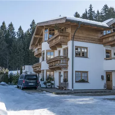 Ein charmantes alpenländisches Haus im Winter mit schneebedecktem Boden. Die Umgebung ist von dichten, grünen Wäldern umgeben.