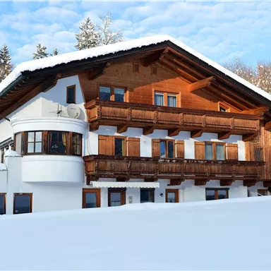 Ein gemütliches Chalet im Schnee mit Holzverkleidung und Balkonen. Umgeben von einem winterlichen Landschaftsbild.