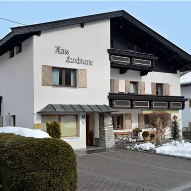 A typical agricultural house with dark wood and a white coat of paint. The snow lies on the ground, and it is a quiet, wintry atmosphere.