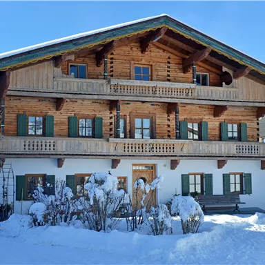 A traditional wooden house with several balconies and green shutters. The entire scene is surrounded by snow and exudes a wintry atmosphere.