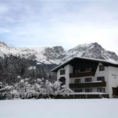 A beautiful house in the snow with mountains in the background. The landscape is wintry and peaceful.